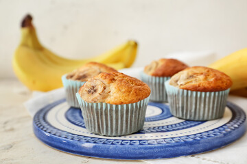 Plate with tasty cupcakes and bananas on light background, closeup