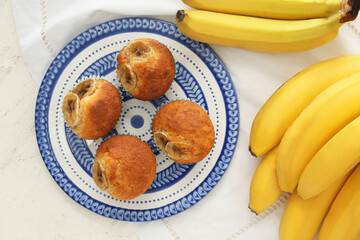 Plate with tasty cupcakes and bananas on light background