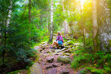 Hipster girl in the mountains. Stylish woman in checkered shirt sitting on stones in forest. Wanderlust concept. Hiking and travelling in summer. mysterious wood. Beautiful nature.