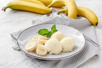 Plate with tasty ice cream and bananas on light background