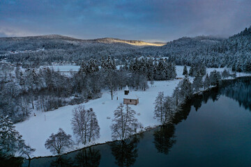 Lever de soleil sur le lac de Longemer et la Chapelle Saint-Clément dans le Massif des Vosges en hiver