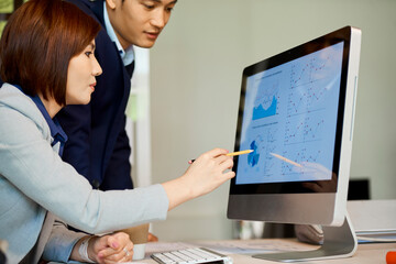 Young pretty Asian businesswoman pointing at diagram on computer screen when discussing report with colleague