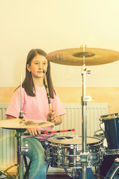 Happy Girl In Music Therapy By Playing Drum Kit On Music Room. Beautiful Young Girl Drummer With Drumsticks Playing Drums And Cymbals. Female Drummer. Toned. Vertical Photo