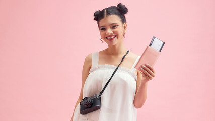 Excited young female tourist with beautiful smile holding passport with tickets, isolated on pink background