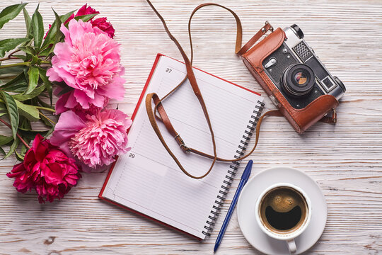 Beauty blog concept. Blogger or freelancer workspace with clipboard, notebook, retro camera, peonies and mobile phone on white bac.