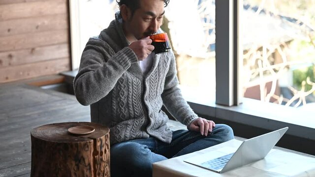 お洒落なウッドデッキでコーヒーを飲みながらリモートで打ち合わせしているお金持ち風の日本人男性