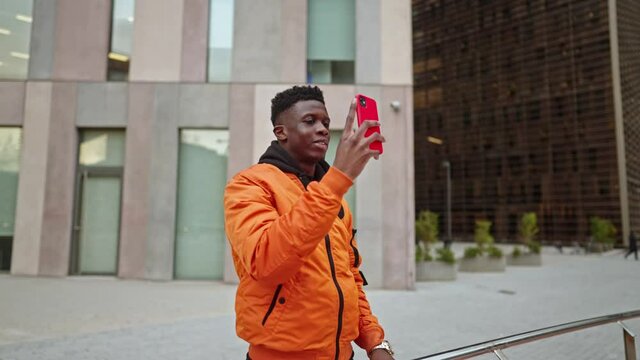 Stylish portrait of a cool black african american mobile photographer in a downtown city center. He takes photos of modern business buildings . Shot in 4k. City exploring