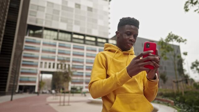 Stylish portrait of a cool black african american man in a downtown city center. He chats a cell phone in online messanger . Shot in 4k. City exploring
