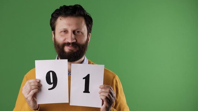 A cheerful white bearded good-looking man in a yellow sweater shows the number 91 on a white sheet. Chrome key, green screen, copy space