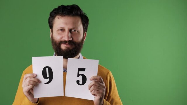 A cheerful white bearded good-looking man in a yellow sweater shows the number 95 on a white sheet. Chrome key, green screen, copy space
