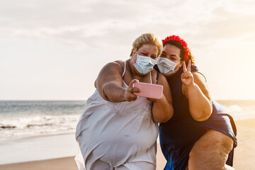 Happy plus size women taking selfie with mobile smartphone on the beach - Overweight friends having fun on vacation during corona virus pandemic - Healthcare and technology concept