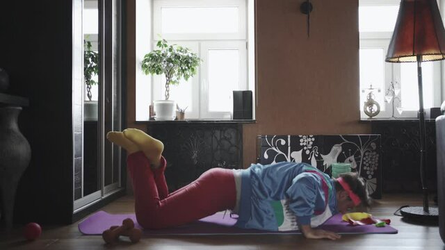 Freak Gay guy doing push-ups at home isolated on a yoga mat, wearing a different color tracksuit and looking 80s style.