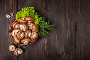 mushrooms in a basket with lettuce and herbs on a dark wooden background topr view