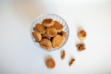 Homemade cookies and walnuts are in a bowl and on a white table. Close-up