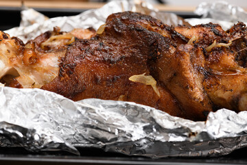 baked meat and fried onions on a baking sheet, pork ham on foil and wooden background, home cooking