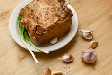 Obraz na płótnie Canvas baked meat on a plate, green onion and garlic on wooden background, home cooking