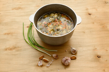 cauldron of soup and garlic on wooden background, home cooking