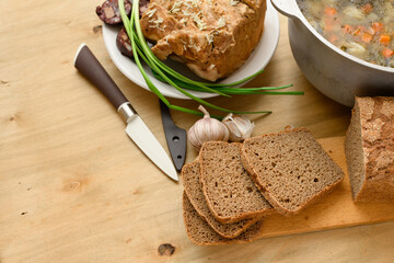 baked meat, soup and blood sausage on a plate, green onion and garlic on wooden background, home...
