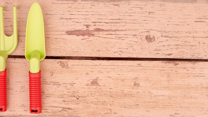 Wide banner with hand garden tools. On the painted planks lie a shovel and a rake with orange...