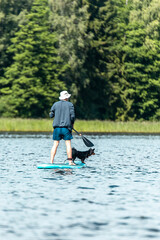 Vertical shot of a man with dog paddling with SUP on paddle board in lake. Vacation concept © Uldis Laganovskis2/Wirestock