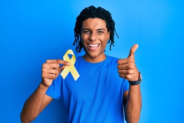 Young african american man holding suicide prevention yellow ribbon smiling happy and positive, thumb up doing excellent and approval sign