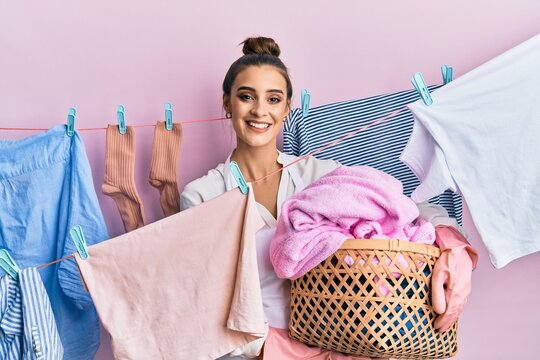 Beautiful brunette young woman holding laundry basket smiling with a happy and cool smile on face. showing teeth.