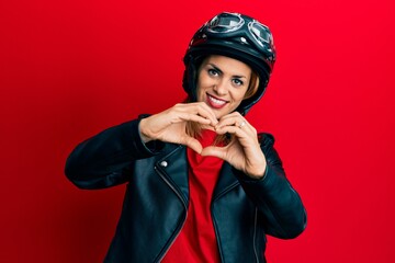 Hispanic young woman wearing motorcycle helmet smiling in love showing heart symbol and shape with hands. romantic concept.