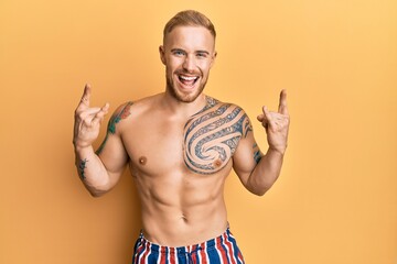 Fototapeta premium Young caucasian man wearing swimwear shirtless shouting with crazy expression doing rock symbol with hands up. music star. heavy concept.