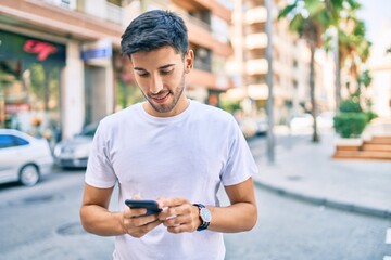 Young latin man smiling happy using smartphone walking at the city.