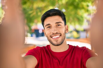 Fototapeta premium Young latin man smiling happy making selfie by the camera at the city.