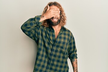 Handsome man with beard and long hair wearing casual clothes smiling and laughing with hand on face covering eyes for surprise. blind concept.