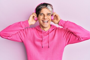 Young hispanic man listening to music using headphones looking positive and happy standing and smiling with a confident smile showing teeth