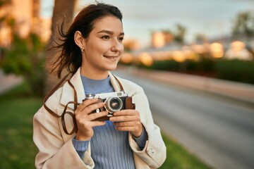 Young hispanic tourist woman smiling happy using vintage camera at the city