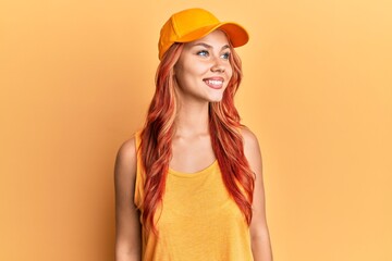 Young beautiful redhead woman wearing casual clothes and yellow cap looking to side, relax profile pose with natural face and confident smile.