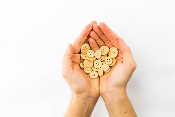 two hands holding a handful of wooden buttons on white background