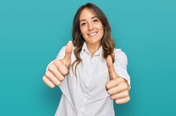 Young brunette woman wearing casual clothes approving doing positive gesture with hand, thumbs up smiling and happy for success. winner gesture.