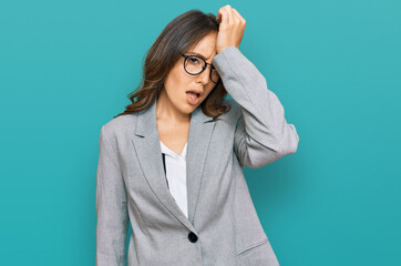 Young brunette woman wearing business clothes surprised with hand on head for mistake, remember...
