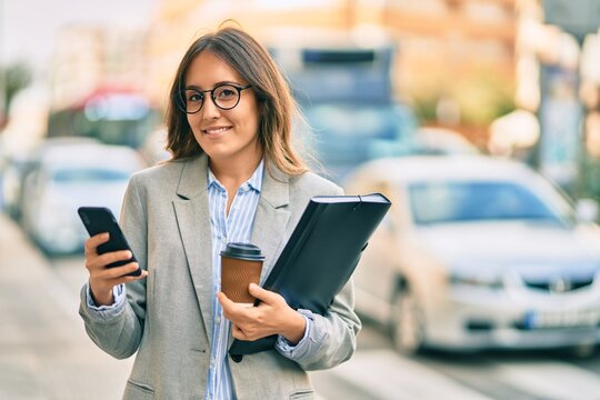Young hispanic businesswoman using smartphone and drinking take away coffee at the city.