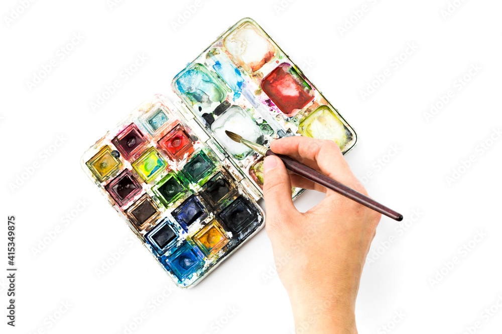 Wall mural box of watercolors of widely used colors with a hand of a woman painter holding a brush to paint, on