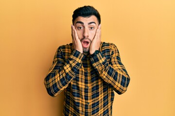 Young hispanic man wearing casual clothes afraid and shocked, surprise and amazed expression with hands on face