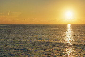 Obraz premium Sun rising above calm sea, clouds coloured to orange