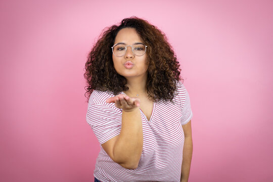 Young african american woman wearing red stripes t-shirt over pink background looking at the camera blowing a kiss with hand on air being lovely and sexy. Love expression.