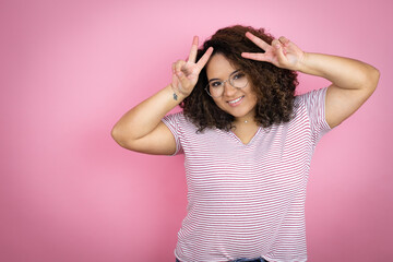Fototapeta premium Young african american woman wearing red stripes t-shirt over pink background Posing funny and crazy with fingers on head as bunny ears, smiling cheerful