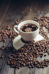 a cup of hot coffee on a wooden table and sprinkled beans close-up