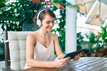 Young beautiful caucasian woman smiling happy at home using touchpad and listening to music wearing headphones