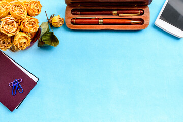 Stationery layout on a blue background. Alarm clock, white postcards, flowers and a smartphone.