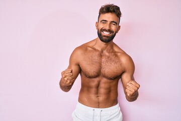 Fototapeta premium Young hispanic man standing shirtless excited for success with arms raised and eyes closed celebrating victory smiling. winner concept.