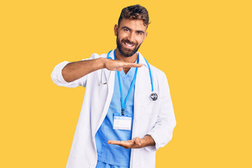 Young hispanic man wearing doctor uniform and stethoscope gesturing with hands showing big and large size sign, measure symbol. smiling looking at the camera. measuring concept.