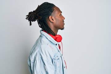 African american man with braids listening to music using headphones looking to side, relax profile pose with natural face with confident smile.