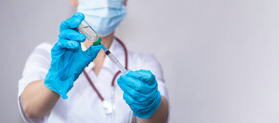 A nurse wearing protective gloves and a mask dials a vaccine into a syringe, the concept of vaccinating the population against coronavirus, influenza, and SARS.